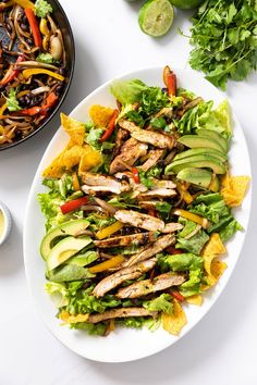 a white plate topped with lettuce, chicken and tortilla chips next to a bowl of salsa