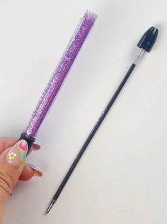 a hand holding a purple and black pen next to a white surface with flowers on it