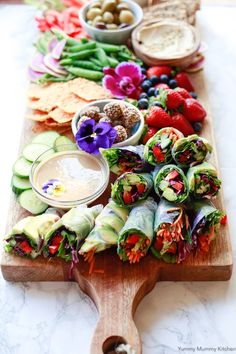 a wooden cutting board topped with veggies and dips on top of a table