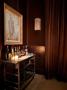 a bar cart with liquor bottles on it in front of a painting