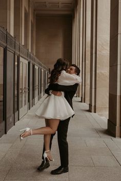 a man and woman are kissing in an empty hallway with columns on either side of them