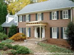 a large brick house with black shutters and white trim on the front door is shown