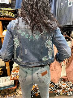 Introducing the epitome of Western elegance: our Denim Jacket adorned with original artwork by the talented Amanda Rose, exclusively printed at The Rodeo Rose shop nestled at the base of South Dakota's majestic Black Hills. This jacket features a captivating hand-tooled leather pattern with turquoise flowers and intricate white scrollwork, creating a stunning fusion of rugged charm and delicate beauty. The pièce de résistance lies on the back: a magnificent turquoise squash blossom, adding a tou Bohemian Printed Outerwear, Fitted Bohemian Printed Outerwear, Spring Hand Painted Denim Jacket, Boot Wallet, Leather Tooling Patterns, Turquoise Squash Blossom, Small Hair Clips, Leather Blazer Jacket, Amanda Rose