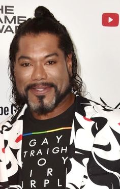 a man with long hair wearing a black and white jacket smiling at the camera while standing in front of a red carpeted wall