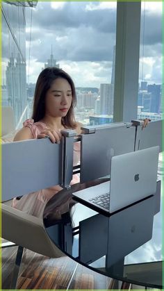 a woman sitting at a table with two laptops in front of her and looking out the window