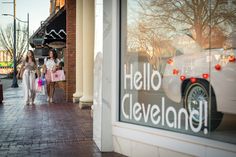 two women are walking down the sidewalk in front of a store window that says hello cleveland