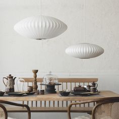 the table is set with plates, cups and teapots in front of two hanging lights