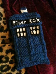 a knitted phone case with the word police box on it sitting on a leopard print blanket