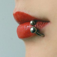 a woman's nose with red lipstick and silver balls attached to the side of her lip