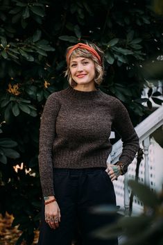 a woman standing in front of a tree wearing a brown sweater and black wide legged pants