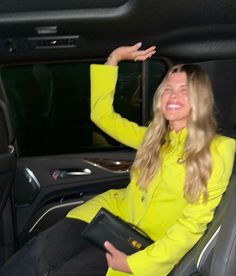 a woman sitting in the passenger seat of a car with her hand up and smiling