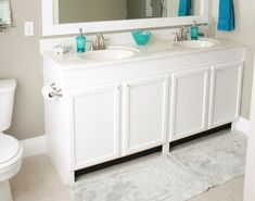 a white bathroom with two sinks and a large mirror above the sink, along with blue towels