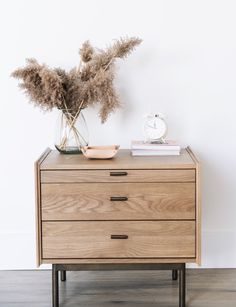 a wooden dresser with two drawers and a clock on the top, in front of a white wall