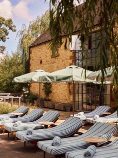 lounge chairs and umbrellas are lined up on the patio outside an old brick building