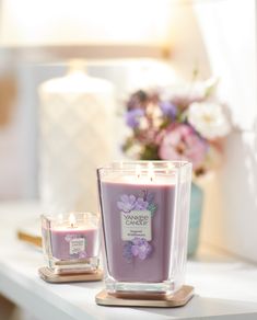 two candles on a table with flowers in the background