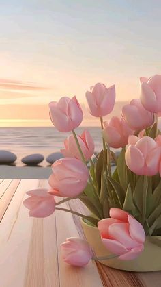 a vase filled with pink flowers sitting on top of a wooden table next to the ocean