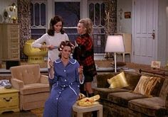 three women standing in a living room with couches and lamps on the sidelines