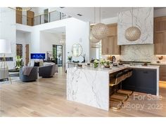 a large open concept kitchen and living room with wood flooring, white marble countertops and cabinets