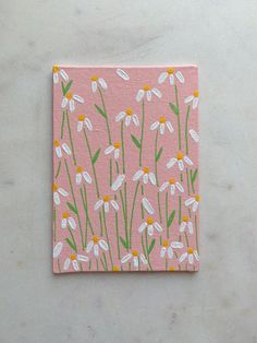 a pink square with white daisies on it and green stems in the center, against a light gray background