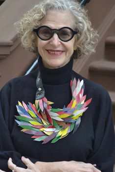 an older woman wearing glasses and a colorful paper wreath around her neck is standing in front of some steps