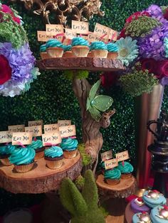 cupcakes are displayed on three tiered trays in front of flowers and greenery