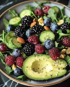 a bowl filled with berries, avocado and spinach on top of a table