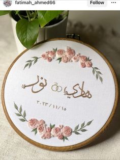 a cross stitch pattern with the words in arabic and pink roses on it, next to a potted plant