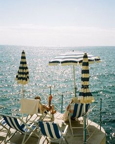 two lounge chairs and an umbrella on the deck of a boat in the ocean with blue water