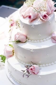 a three tiered white cake with pink flowers on the side and pearls around the edges