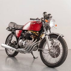 a red and black motorcycle parked on top of a cement floor next to a white wall