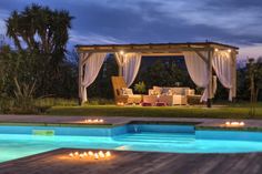 an outdoor pool with candles lit up in the evening and a gazebo behind it