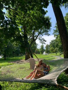 two women are sitting in a hammock on the grass and one is holding her baby