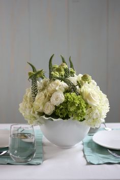 a white bowl filled with flowers on top of a table next to plates and silverware