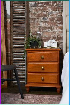 a wooden dresser sitting next to a bed in a room with brick walls and windows