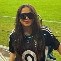 a woman with sunglasses on standing in front of a soccer field wearing a number 8 t - shirt