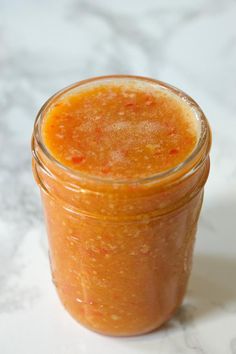 a jar filled with orange colored liquid on top of a white countertop next to a spoon