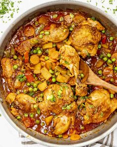 a pot filled with chicken and vegetables on top of a white table cloth next to a wooden spoon