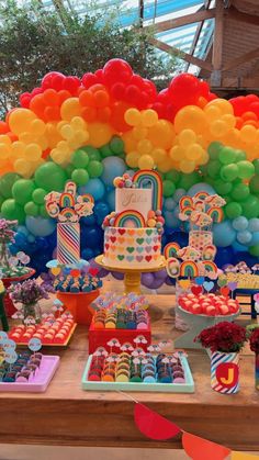 a table topped with lots of colorful balloons and desserts on top of it's sides