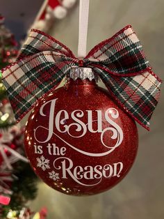 a red ornament hanging from a christmas tree that says jesus is the reason