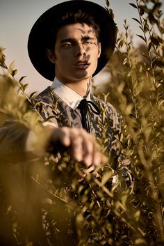 a young man wearing a black hat and tie standing in the middle of tall grass