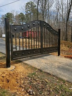 an iron gate in the middle of a dirt area with trees and grass around it