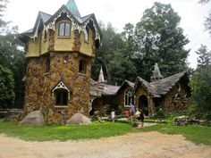 people are standing in front of an unusual house made out of rocks and stone blocks