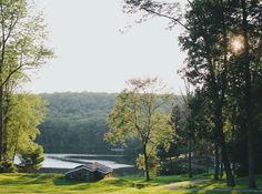 a lake surrounded by trees and grass in the middle of a forest with sun shining on it