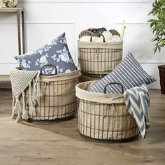 three baskets with pillows and blankets on the floor