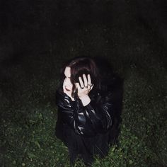 a woman is covering her face with her hands in the grass at night while holding her hand up to her face