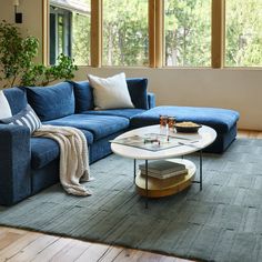 a living room with blue couches and coffee table in front of two large windows