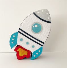 a paper rocket ship sitting on top of a white table next to a red and blue object