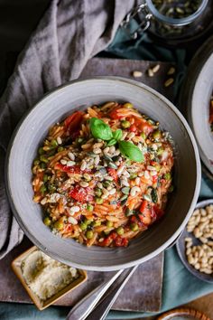 two bowls filled with pasta and vegetables on top of a wooden table next to bread