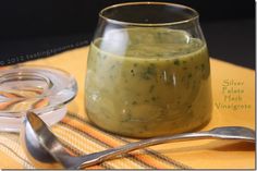 a glass jar filled with green sauce next to two spoons on top of a table