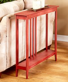 a red end table sitting on top of a wooden floor next to a white couch